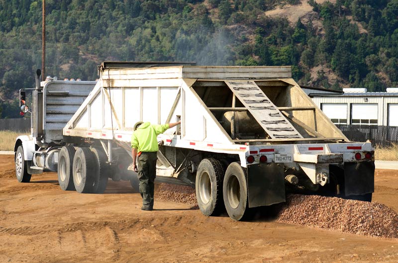 View of a belly dumper trailer depositing material at a construction site, like the services offered by Oden Transport in Texas.