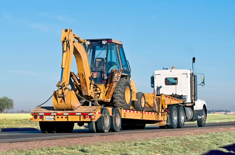View of a heavy equipment backhoe being hauled in Texas near Amarillo or Lubbock, like the services offered by Oden Tranport.