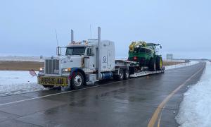 Large farm tractor being hauled during snowy weather on trailer by Oden Transport, with services in Texas, Oklahoma, Kansas & New Mexico.